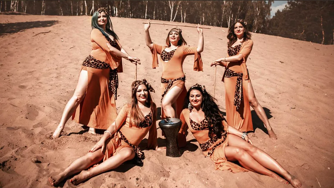 Pięć kobiet na plaży. Wszystkie ubrane są w jednakowe stroje do tańca.