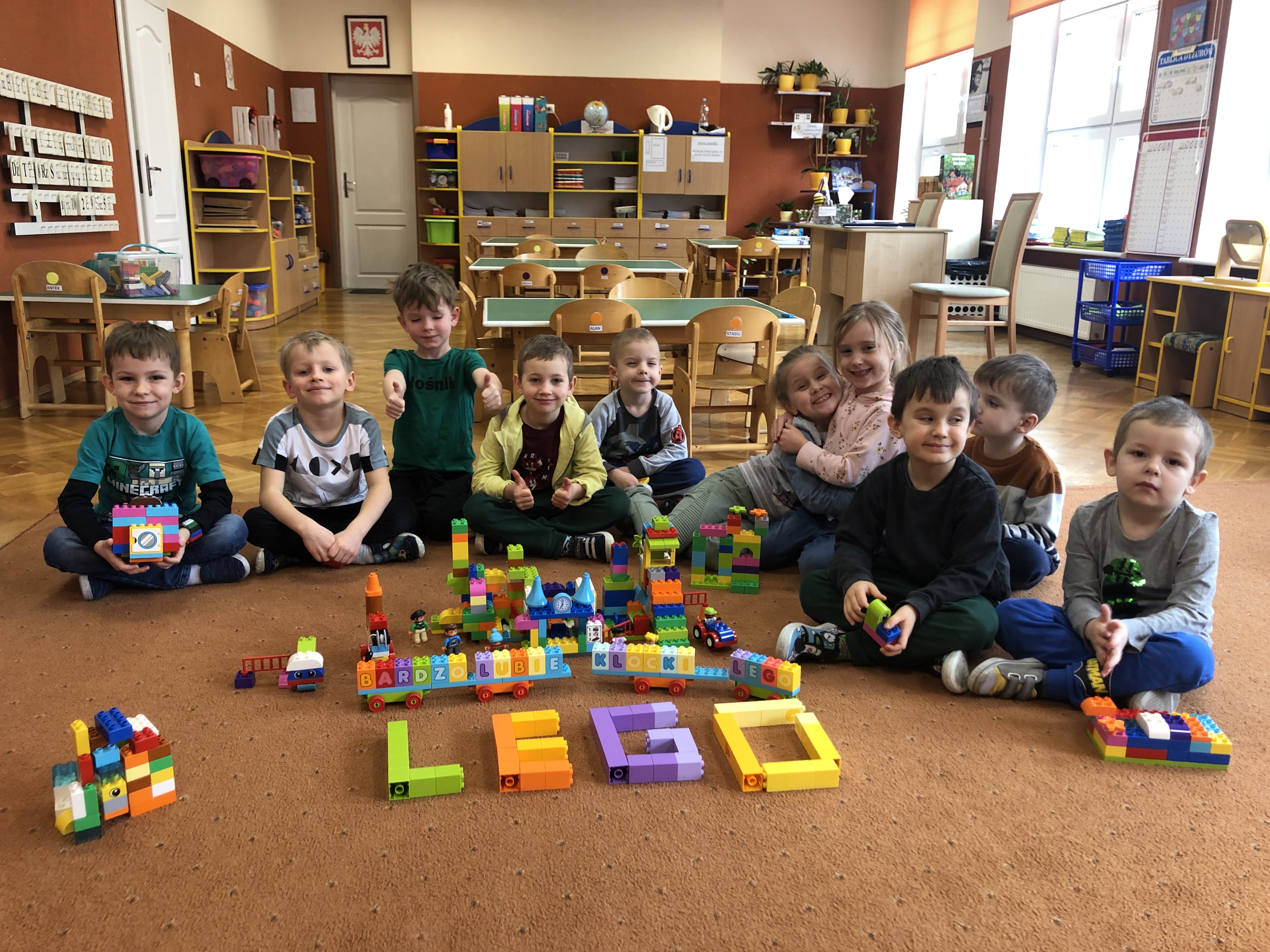 Dziesięcioro dzieci na dywanie. Różne przedmioty zbudowane z klocków Lego.