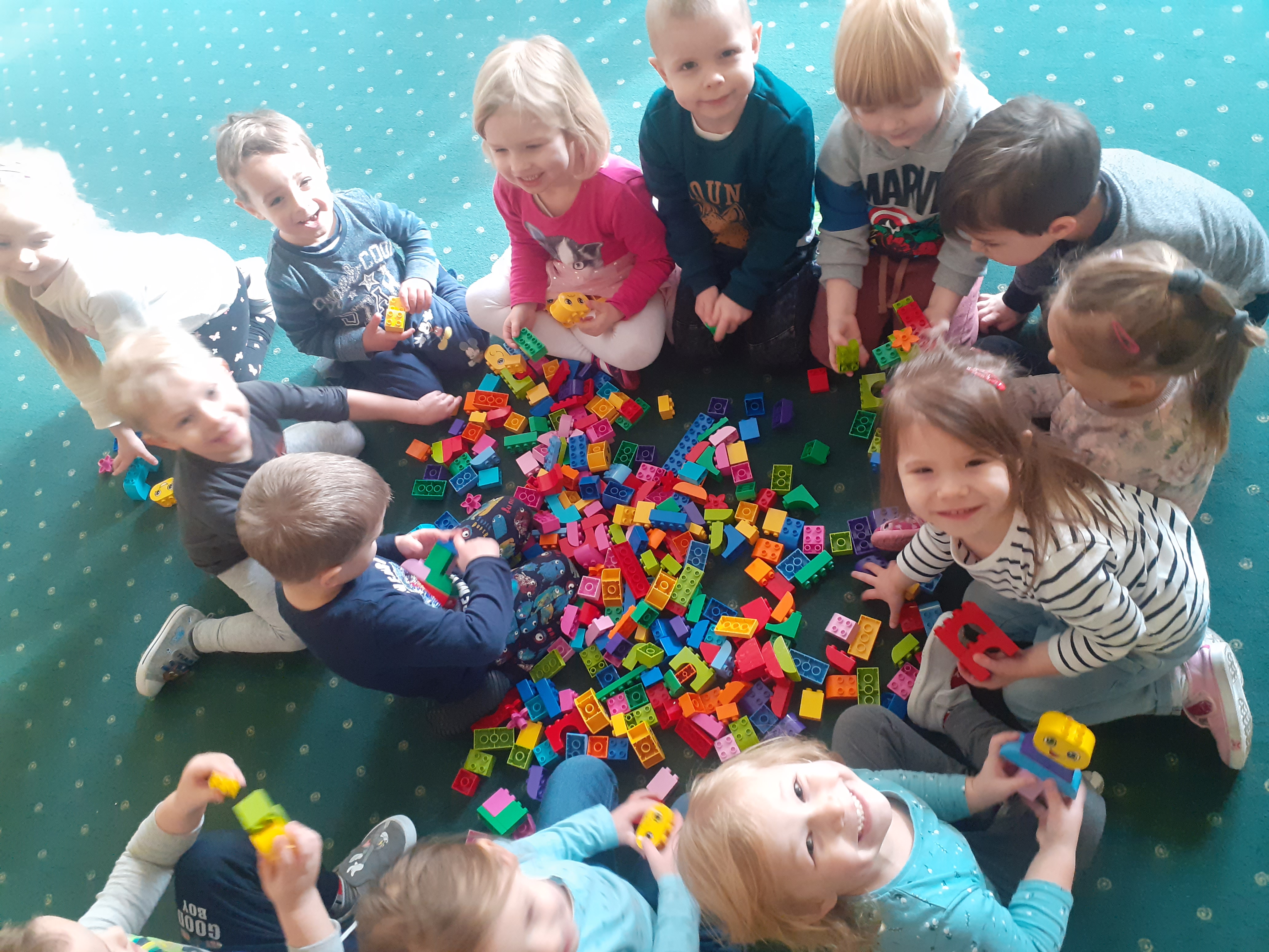 Dziesięcioro dzieci na dywanie. Rozsypane klocki Lego.