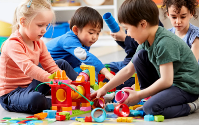 Dzieci siedzące na dywanie, bawiące się kolorowymi klockami lego duplo. źródło fot. WWW.LEGO.COM