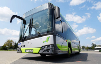 Autobus miejski stojący na parkingu, nad nim błękitne niebo z białymi chmurami. Zdjęcie z pozycji żaby.