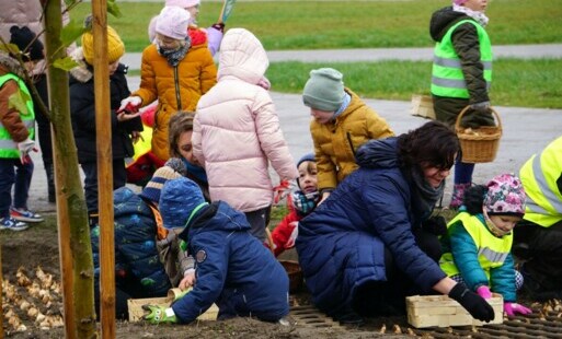 Grupa dzieci i dorosłych sadzących cebulki roślin na skwerze