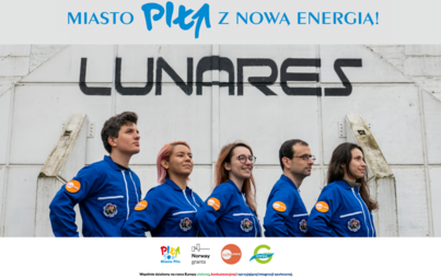 Pięć osób ubranych w jednakowe niebieskie kombinezony kosmonautów stoi przed białym hangarem. Nad nimi na grafice napis: Miasto Piła z nową energią.